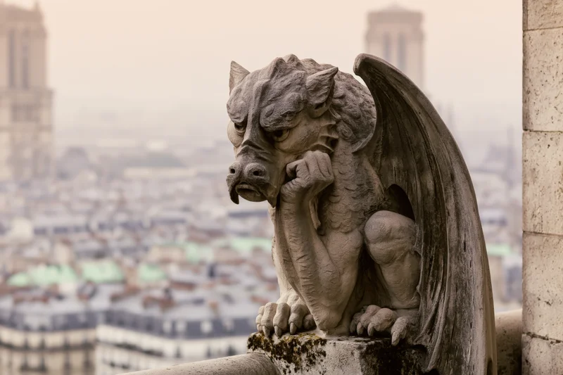 Stone gargoyle sculpture perched on cathedral ledge overlooking Paris cityscape