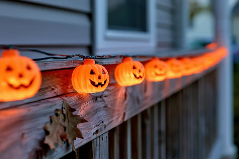 String of glowing plastic jack-o-lantern lights along wooden porch railing at twilight