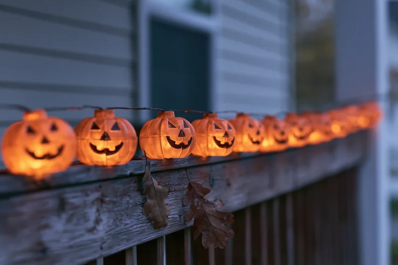 String of glowing plastic jack-o-lantern lights along wooden porch railing at twilight