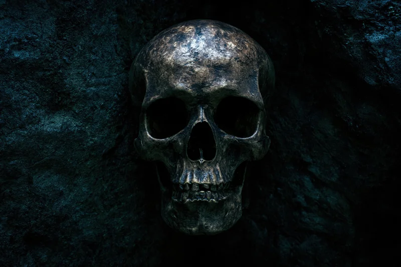 Weathered human skull resting against rough stone wall in dark cave setting