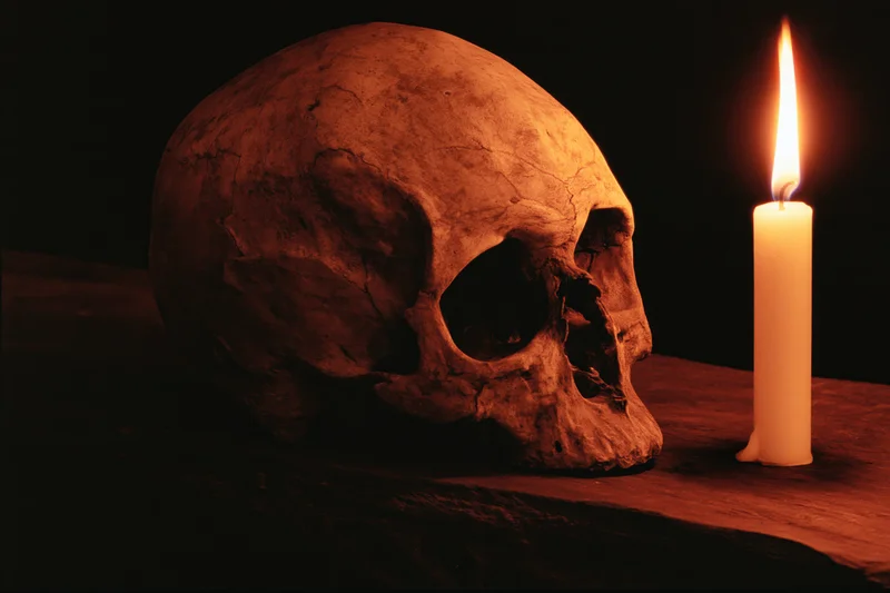 Weathered human skull beside a lit candle on dark wooden surface