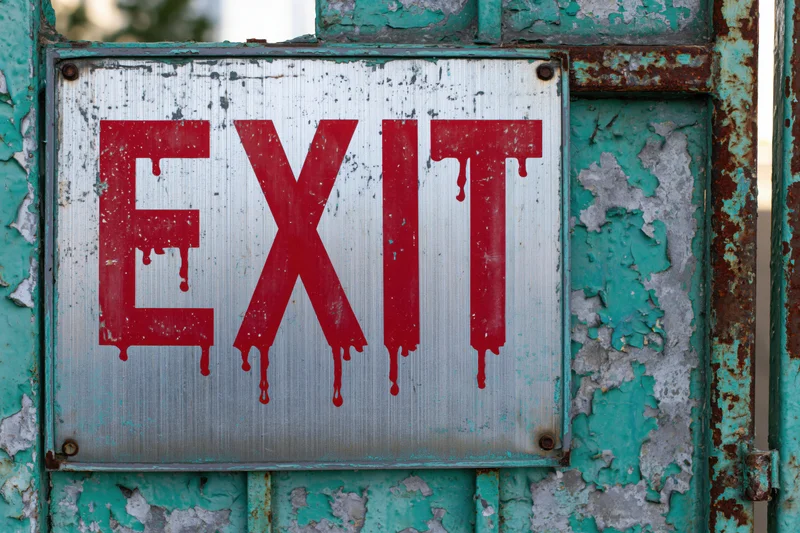 Weathered metal exit sign with red dripping paint mounted on a rusted turquoise door frame