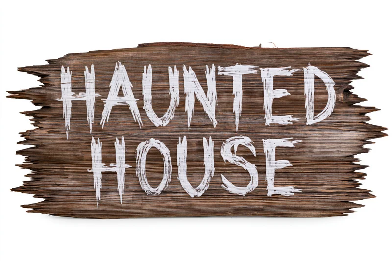 Weathered wooden plank sign with hand-painted white text reading haunted house isolated on white