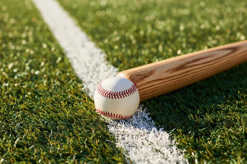 Baseball and wooden bat resting on grass field near white line