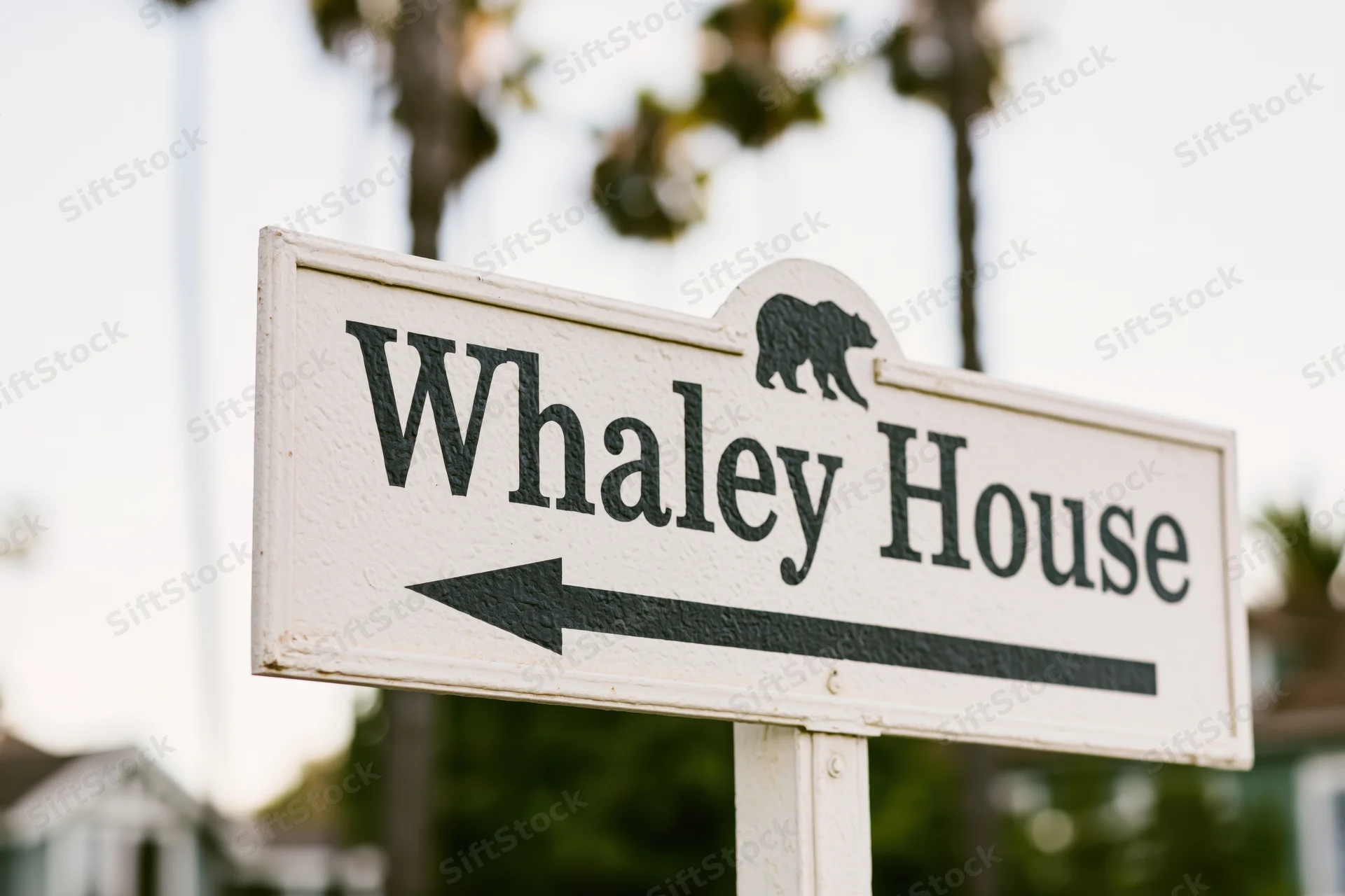 White directional sign for Whaley House with bear symbol and left arrow pointing to landmark in outdoor setting