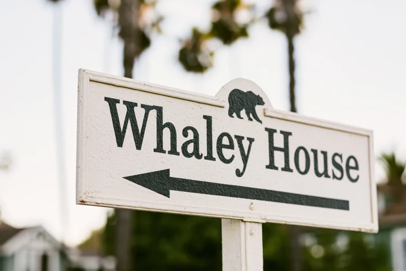 White directional sign for Whaley House with bear symbol and left arrow pointing to landmark in outdoor setting