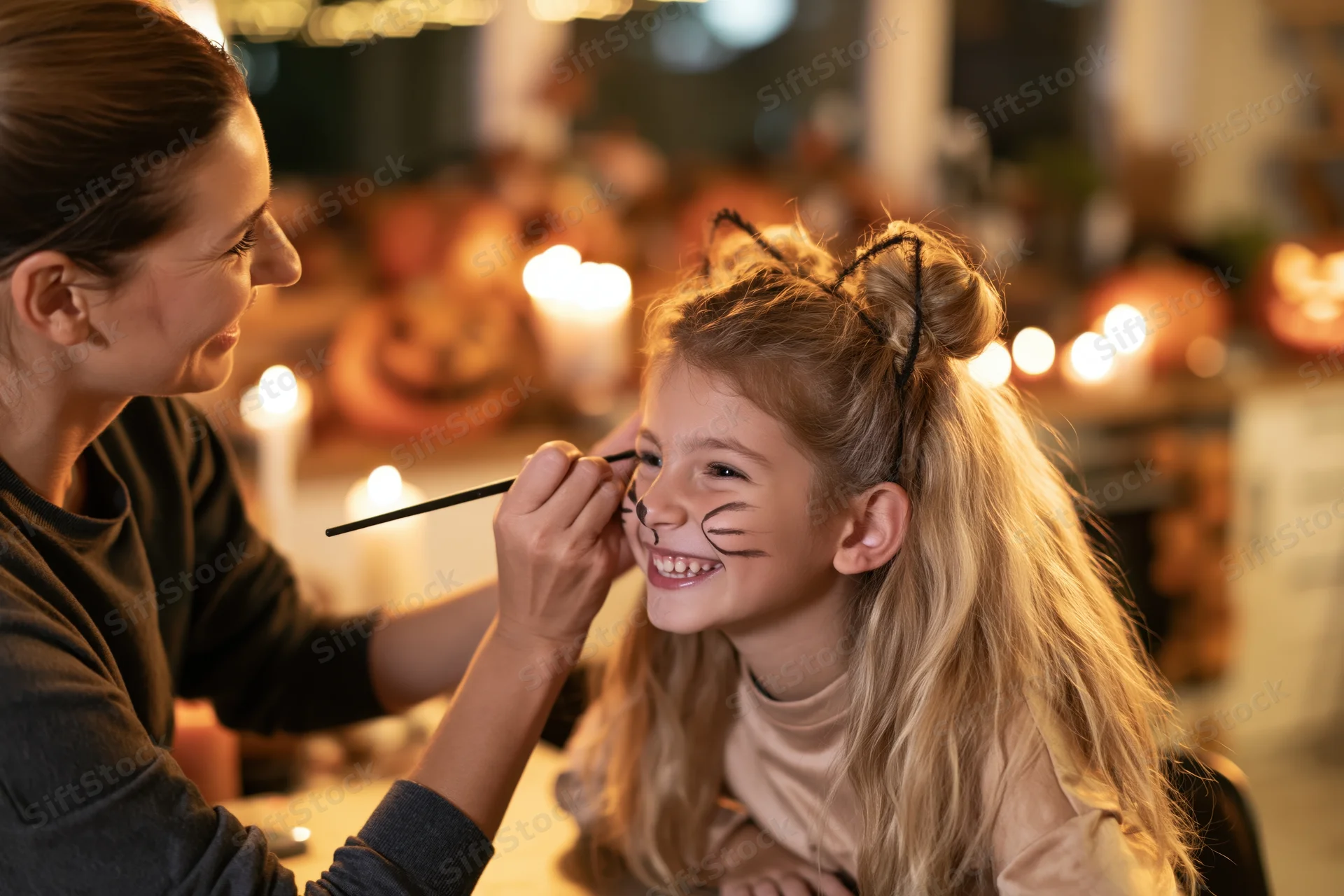 Woman applying face paint to a smiling young girl at home during halloween evening