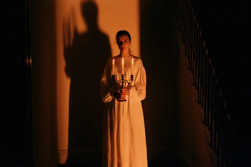 Woman in long white nightgown holding candelabra in dark hallway