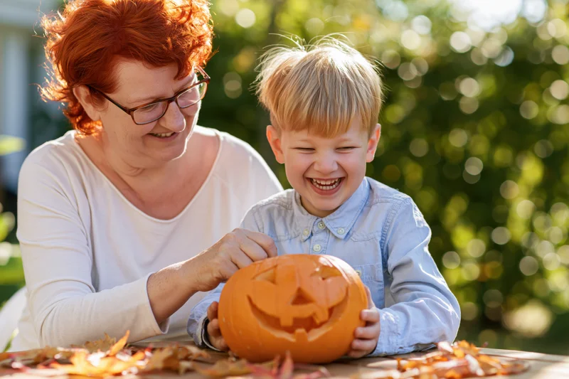 Woman and young boy carving a pumpkin together outdoors in autumn