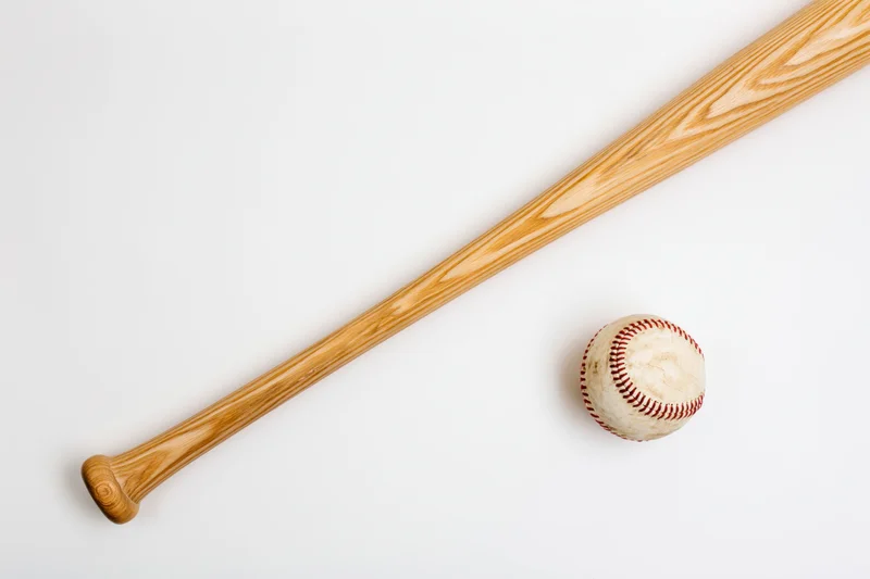 Wooden baseball bat and baseball resting diagonally on white surface