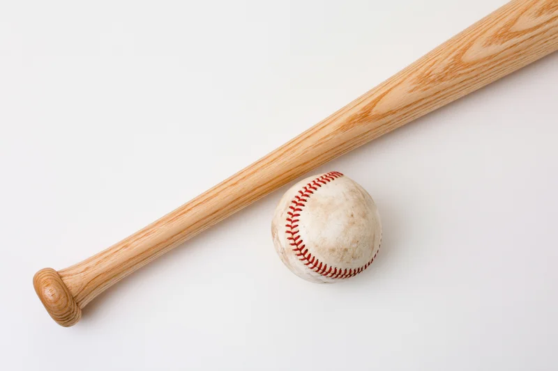 Wooden baseball bat resting diagonally beside a used baseball on white background