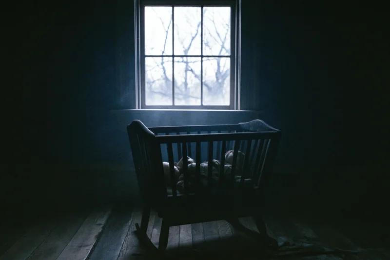 Antique wooden baby cradle in dim abandoned room with light from window