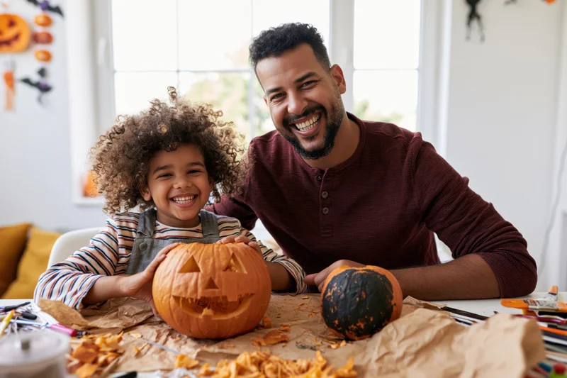 Father and child smiling while carving a pumpkin together at home