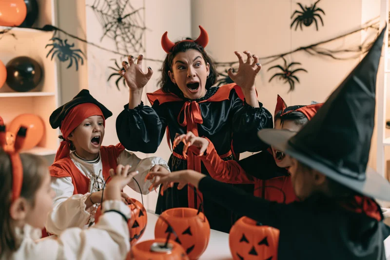 Woman in devil costume with children in halloween costumes at indoor party with pumpkins and decorations