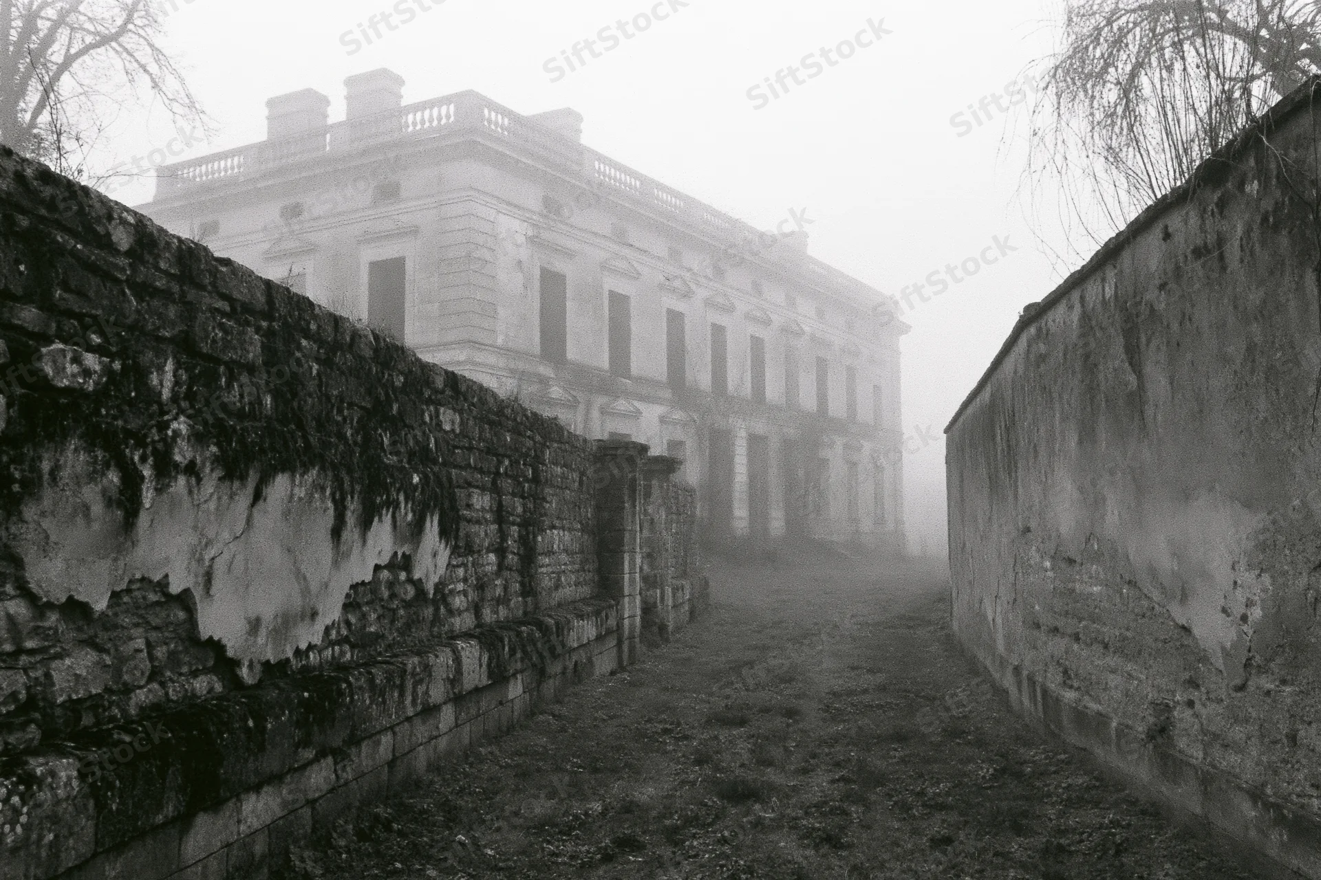Abandoned neoclassical manor viewed through fog along a stone-walled pathway