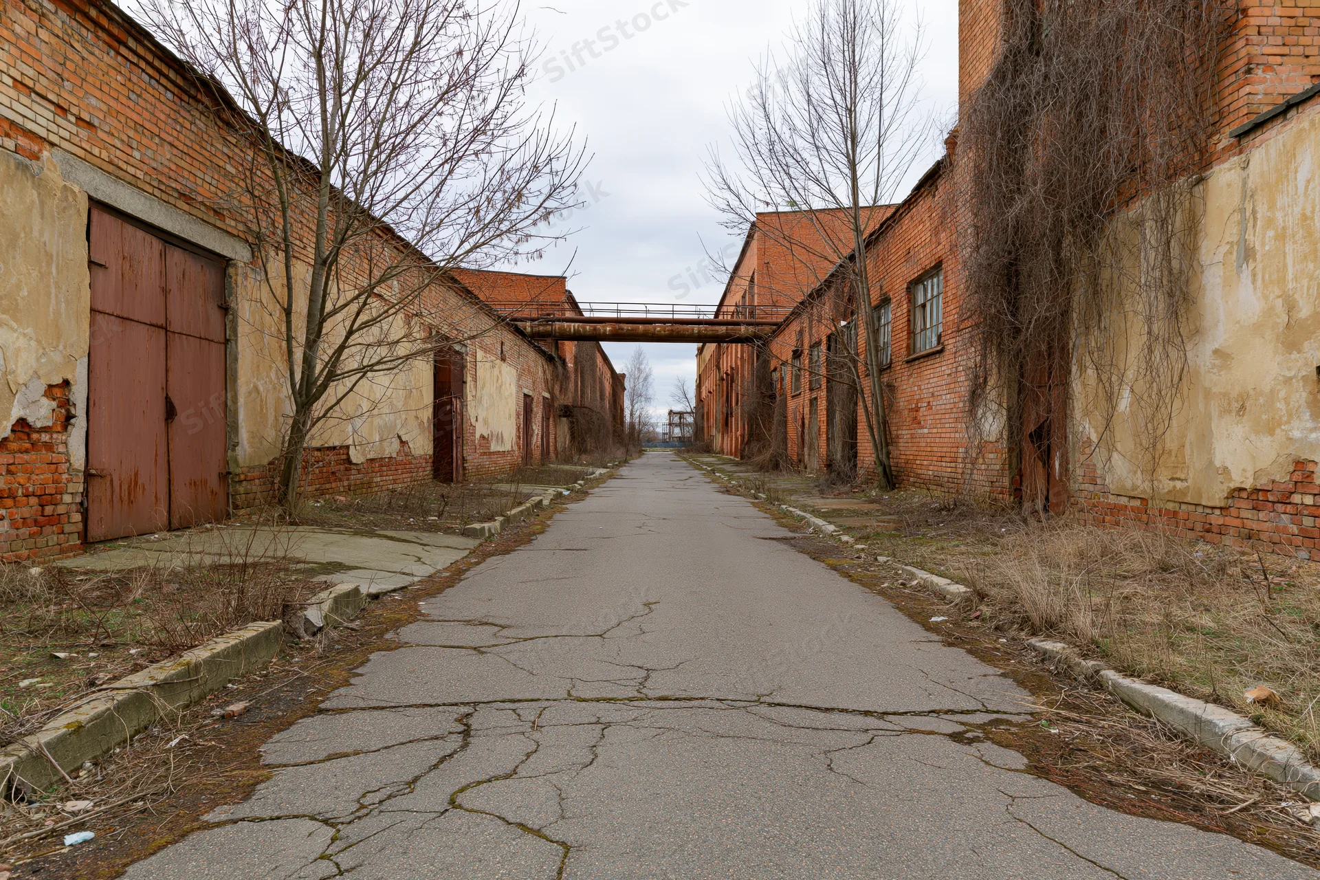 Cracked asphalt pathway between dilapidated brick buildings in an abandoned soviet-era industrial complex