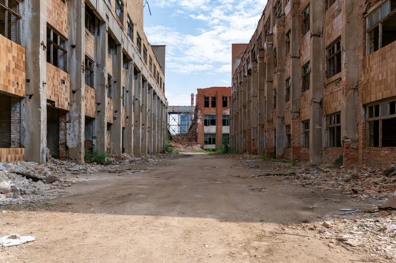Symmetrical dirt courtyard between dilapidated soviet-era industrial buildings under a cloudy sky