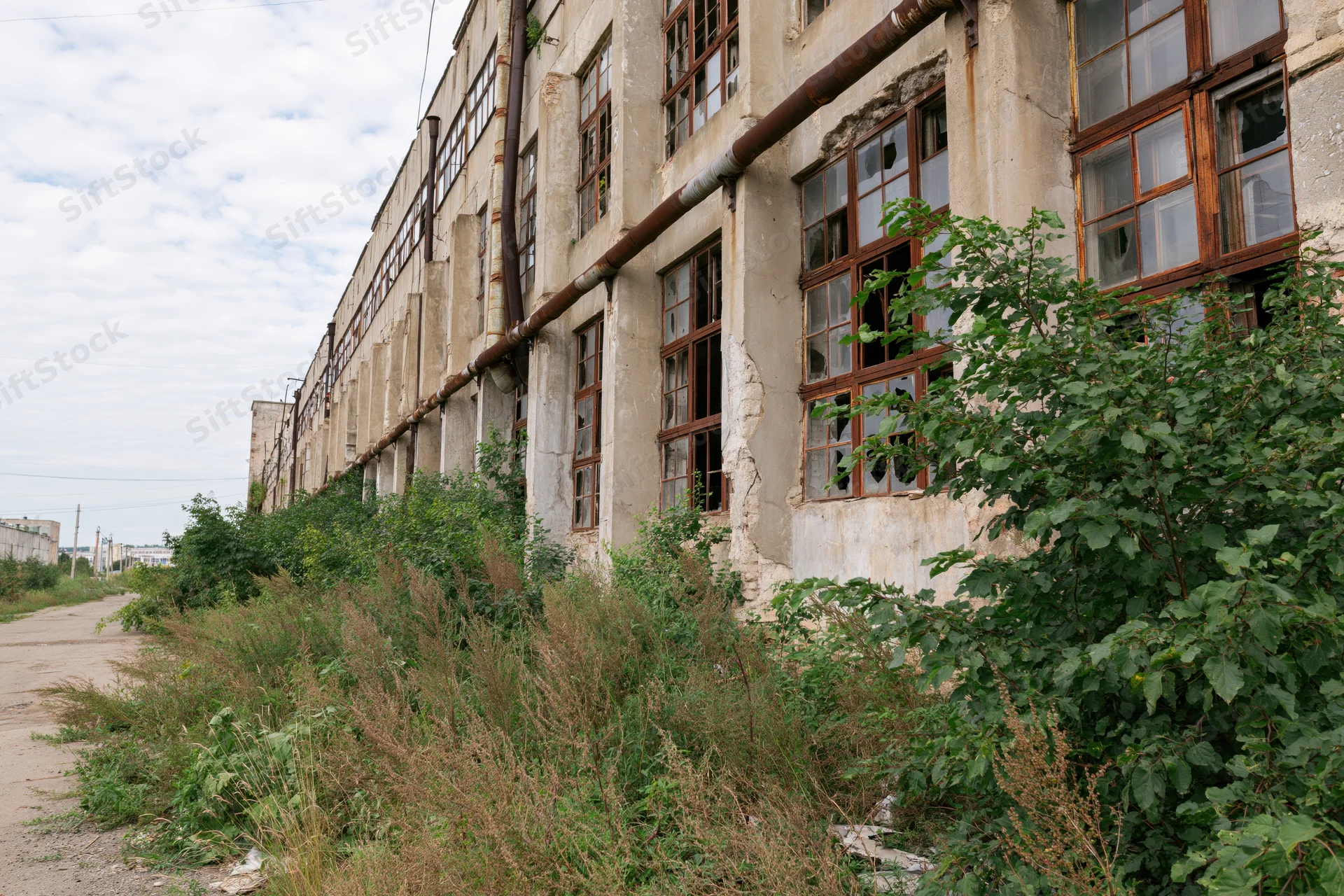 Long abandoned soviet-era industrial factory building with overgrown vegetation along its weathered facade