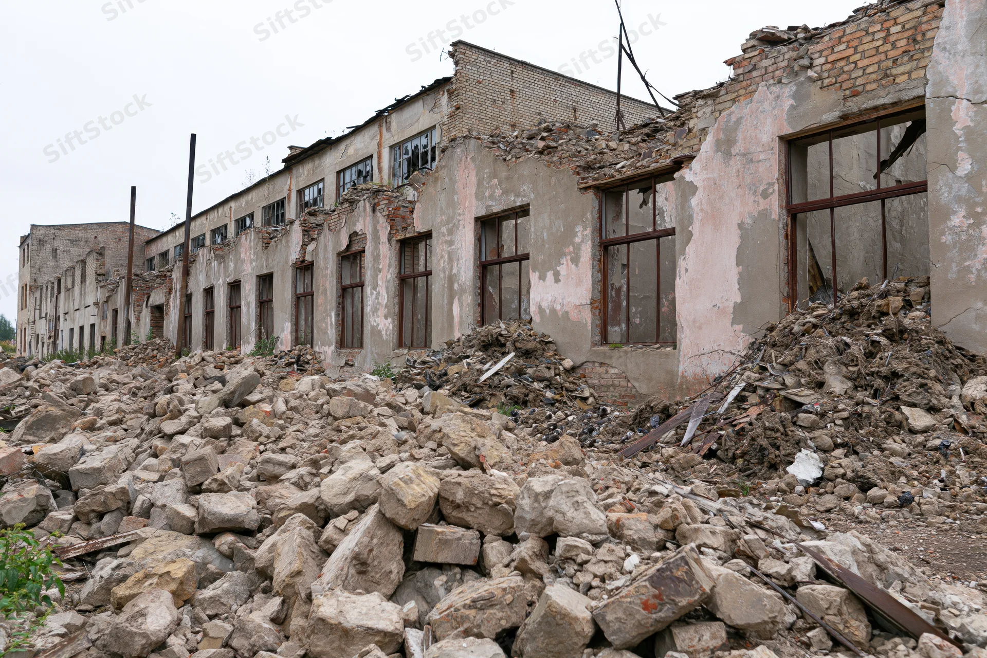 Abandoned soviet-era factory building with crumbling walls and rubble piles in front