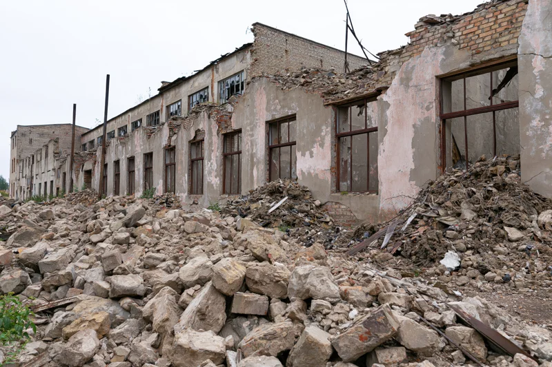 Abandoned soviet-era factory building with crumbling walls and rubble piles in front