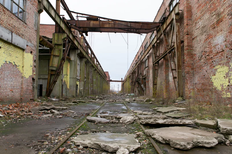Abandoned soviet-era industrial factory complex with rusted metal beams and broken railway tracks between brick walls