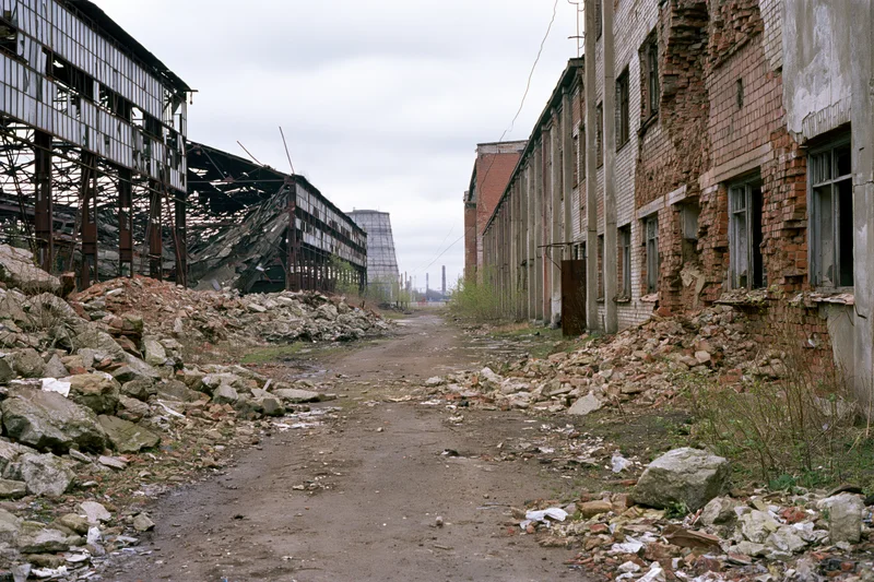 Symmetrical view of abandoned soviet industrial complex with crumbling buildings and rubble-lined pathway