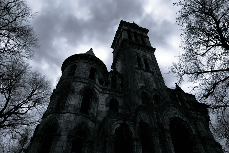 Low-angle view of an abandoned victorian gothic mansion with ivy-covered stone facade and bare trees under overcast sky