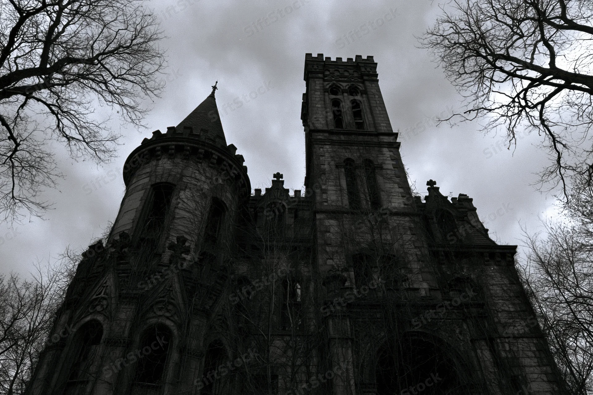 Low-angle view of abandoned victorian gothic mansion with stone towers and bare trees against cloudy sky