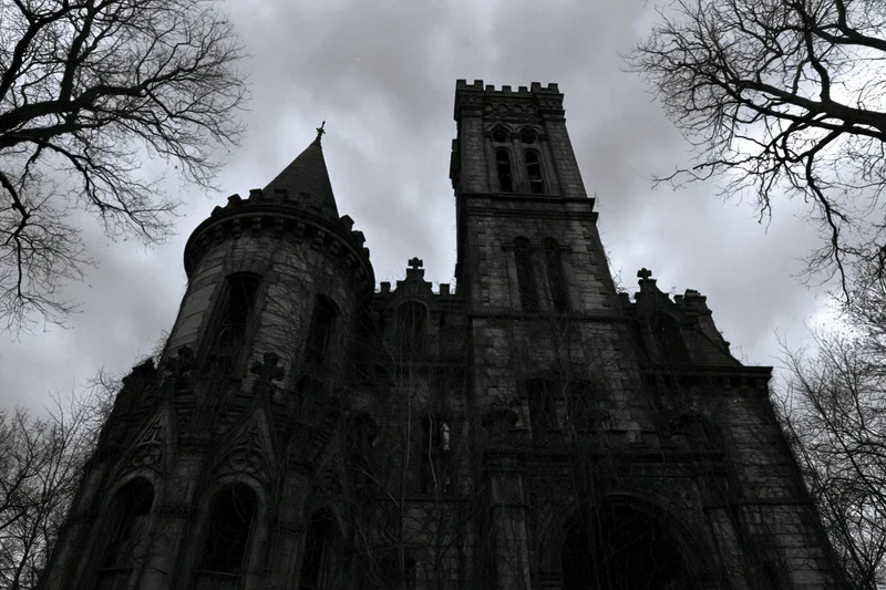 Low-angle view of abandoned victorian gothic mansion with stone towers and bare trees against cloudy sky