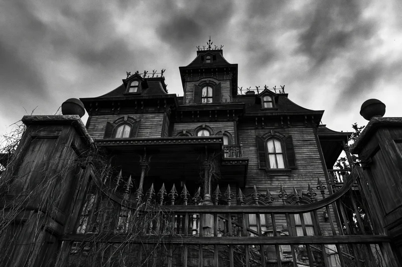 Abandoned victorian mansion with ornate gate and stormy sky viewed from low angle