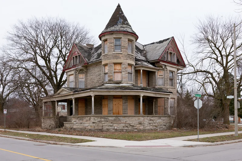 Abandoned victorian mansion with corner turret and boarded windows on a street corner