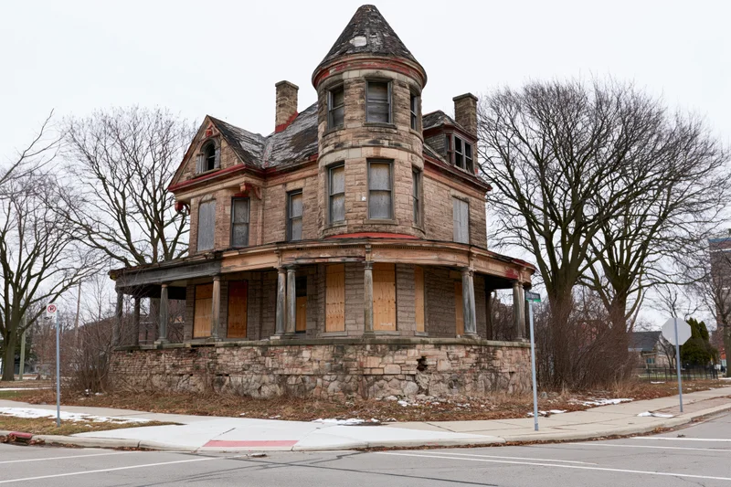 Abandoned victorian mansion with corner turret and boarded windows on a city street corner
