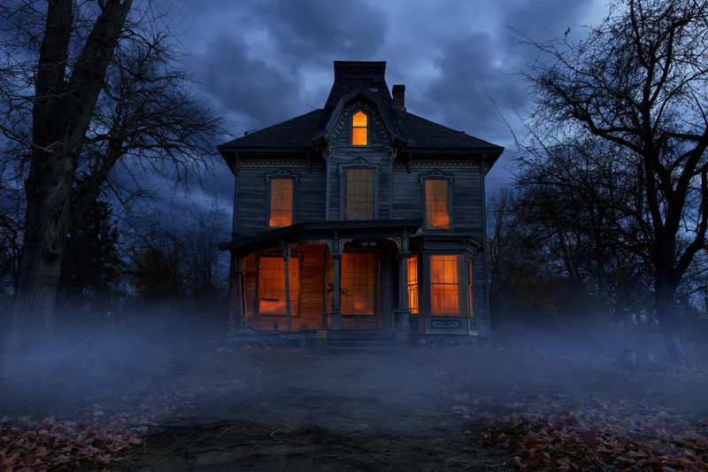 Abandoned victorian house glowing orange at night surrounded by fog and bare trees