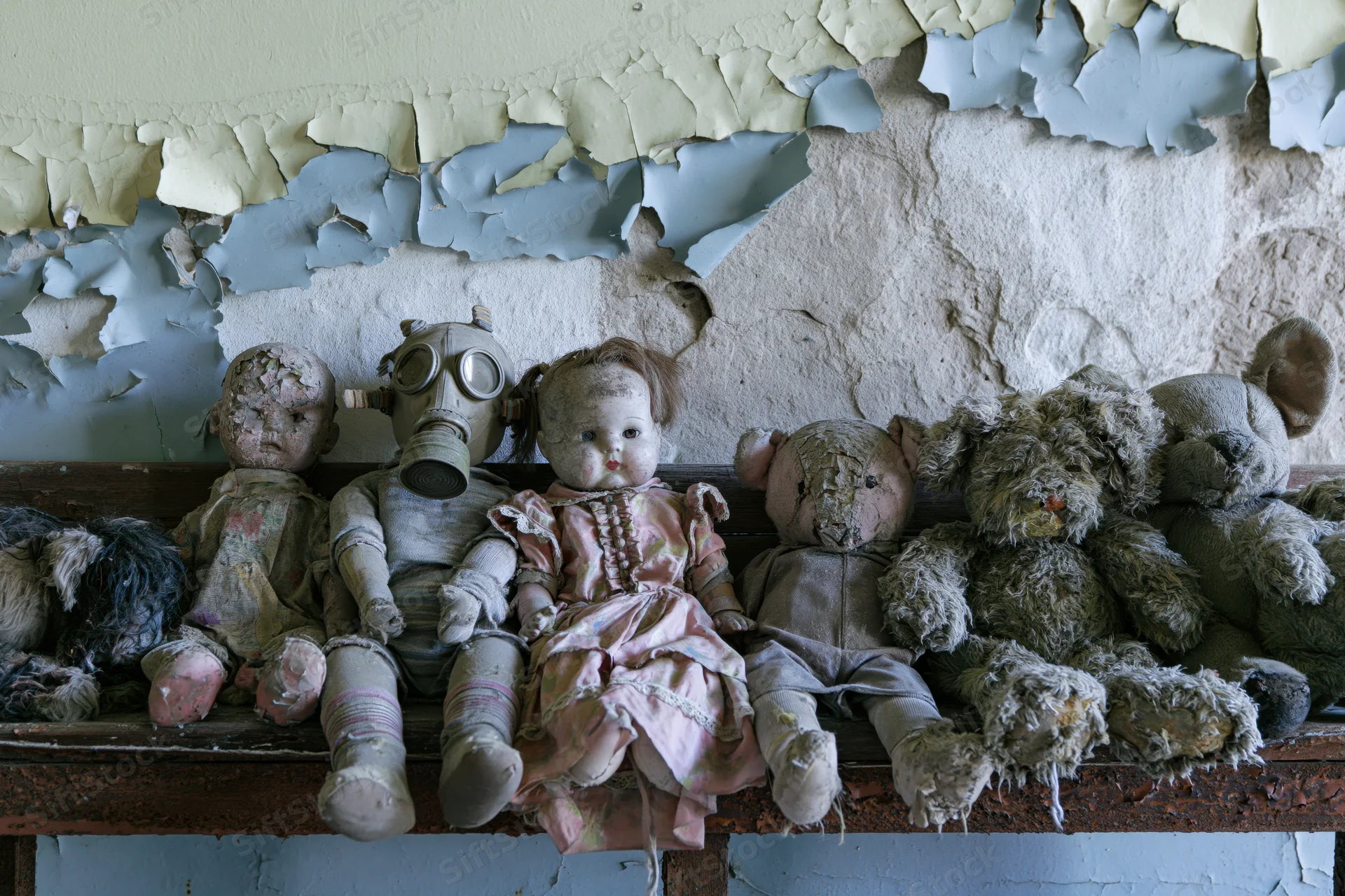 Row of decayed children's toys including dolls and stuffed animals on a shelf beneath peeling paint