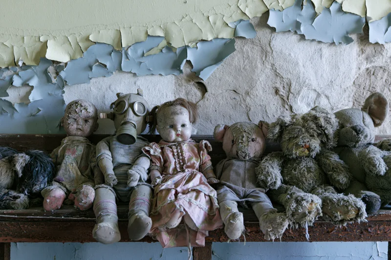 Row of decayed children's toys including dolls and stuffed animals on a shelf beneath peeling paint