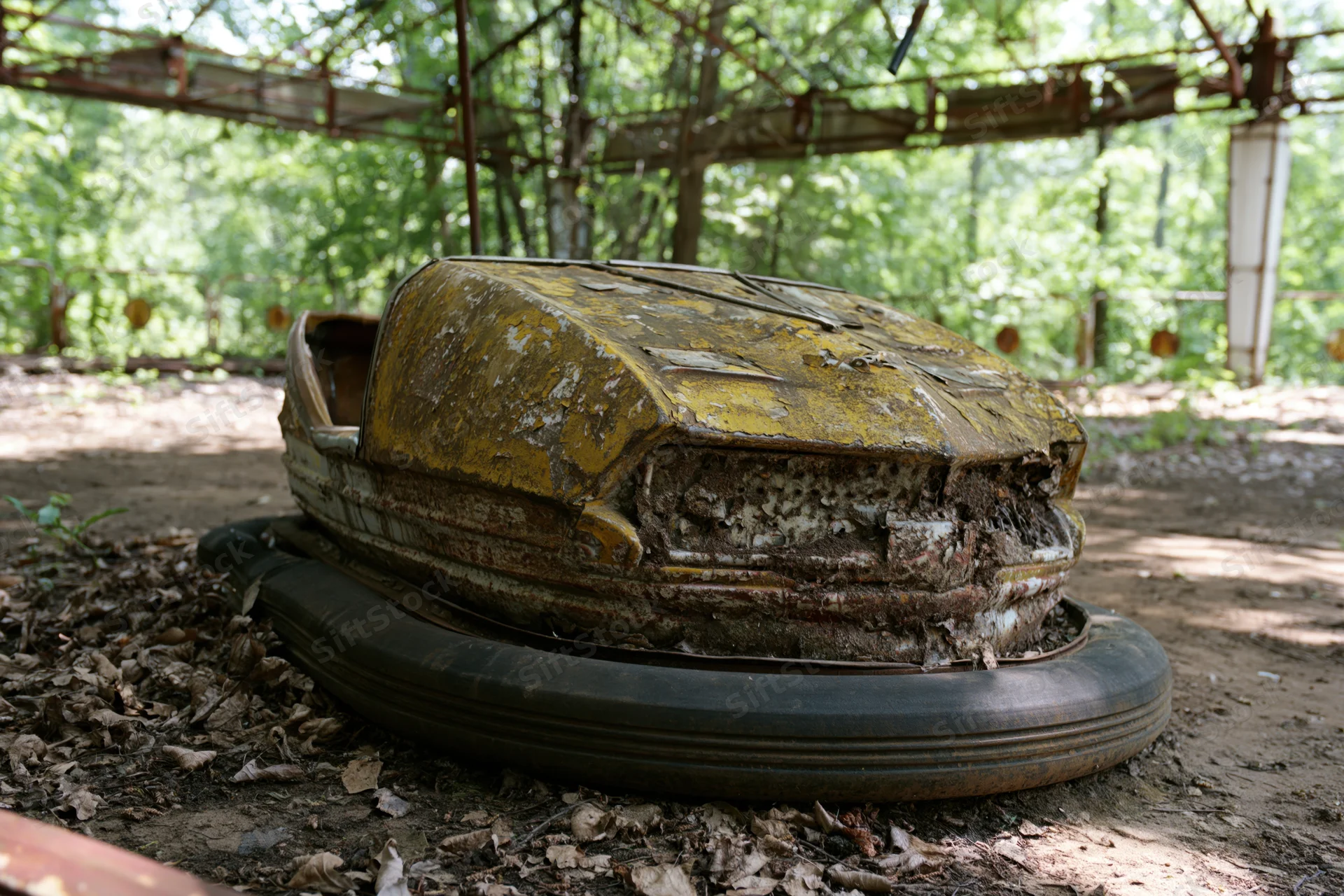 Decayed yellow bumper car resting on dirt floor under metal canopy in overgrown amusement park area