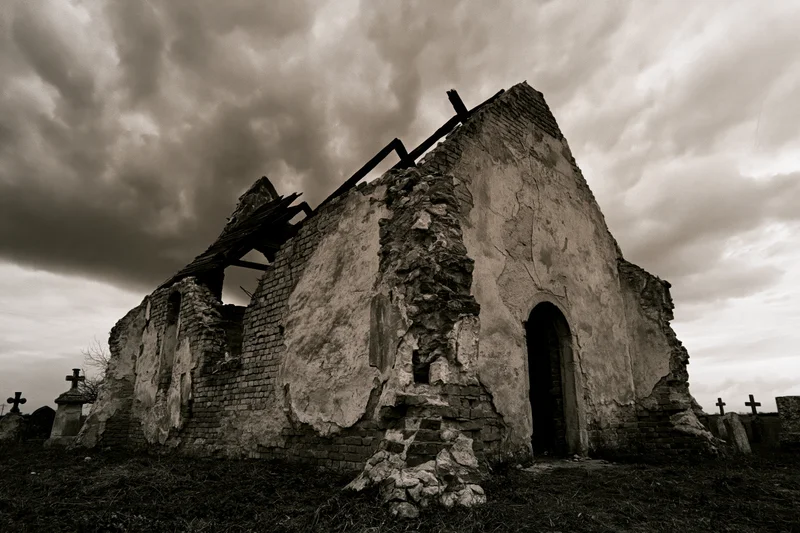 Crumbling stone chapel with collapsed roof in a cemetery under cloudy sky