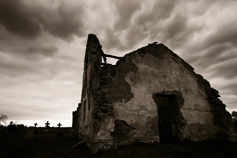 Crumbling stone chapel ruin with collapsed roof in a cemetery under stormy sky