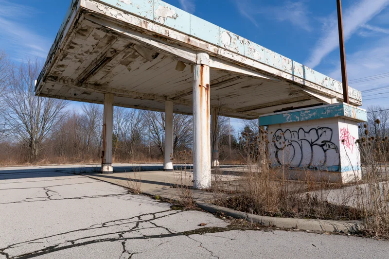 Abandoned gas station with crumbling canopy and graffiti under a clear blue sky