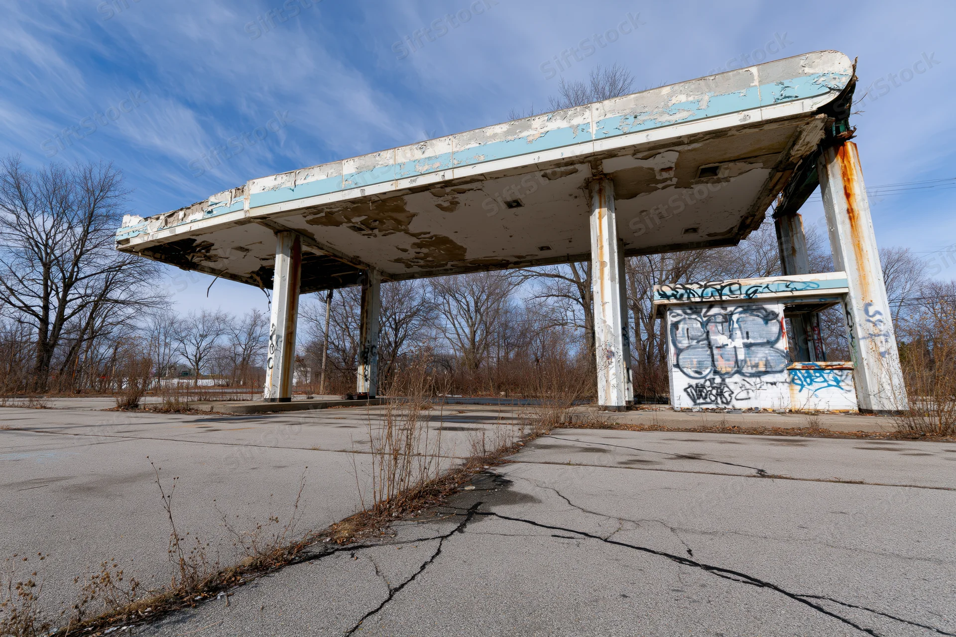 Abandoned gas station with crumbling canopy and graffiti under a blue sky