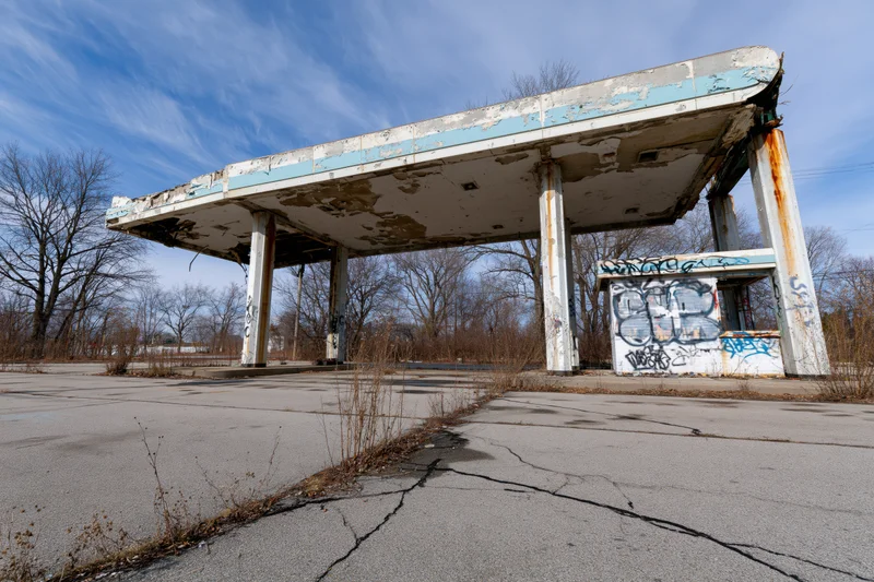 Abandoned gas station with crumbling canopy and graffiti under a blue sky