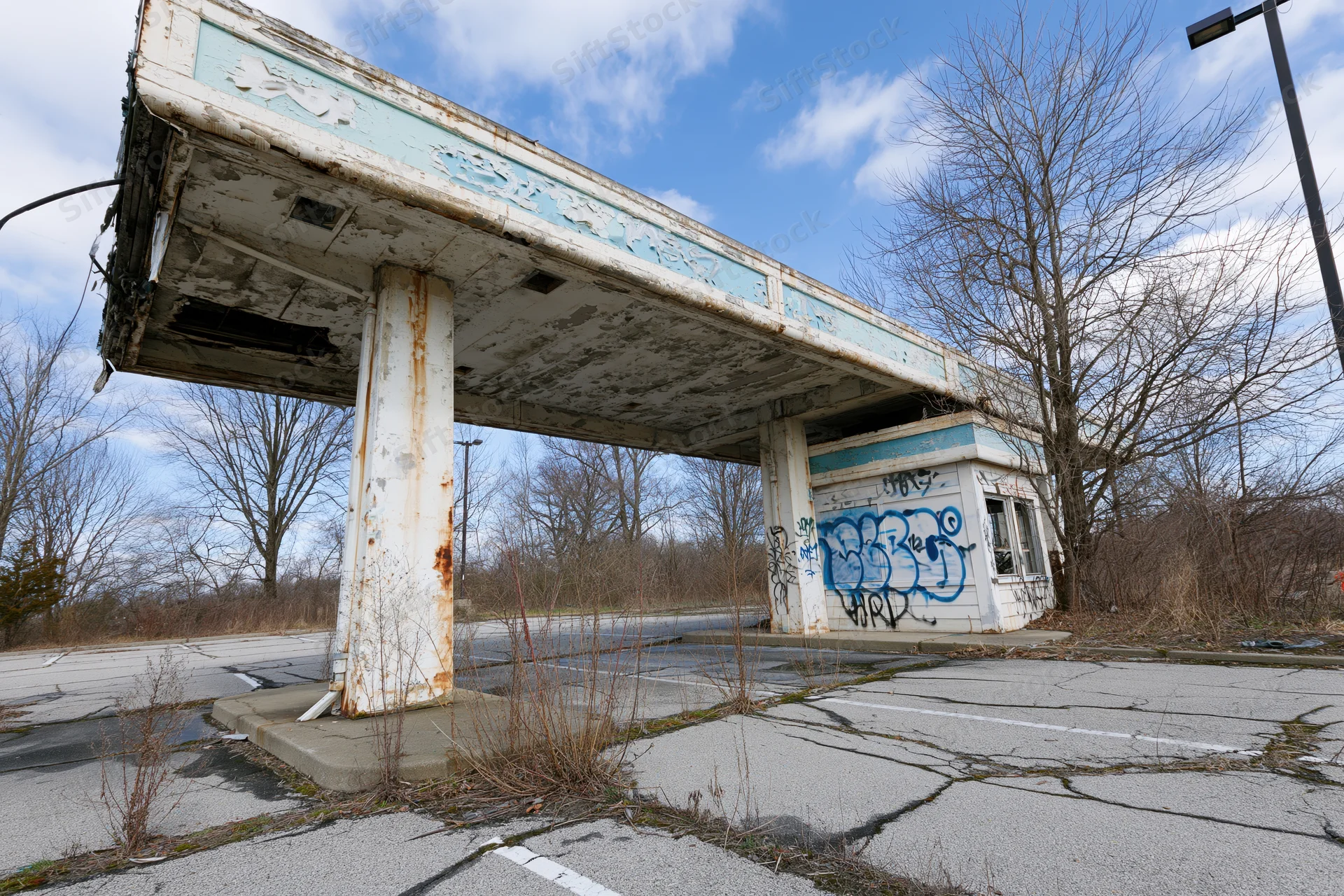 Abandoned gas station with crumbling canopy and graffiti under a blue sky