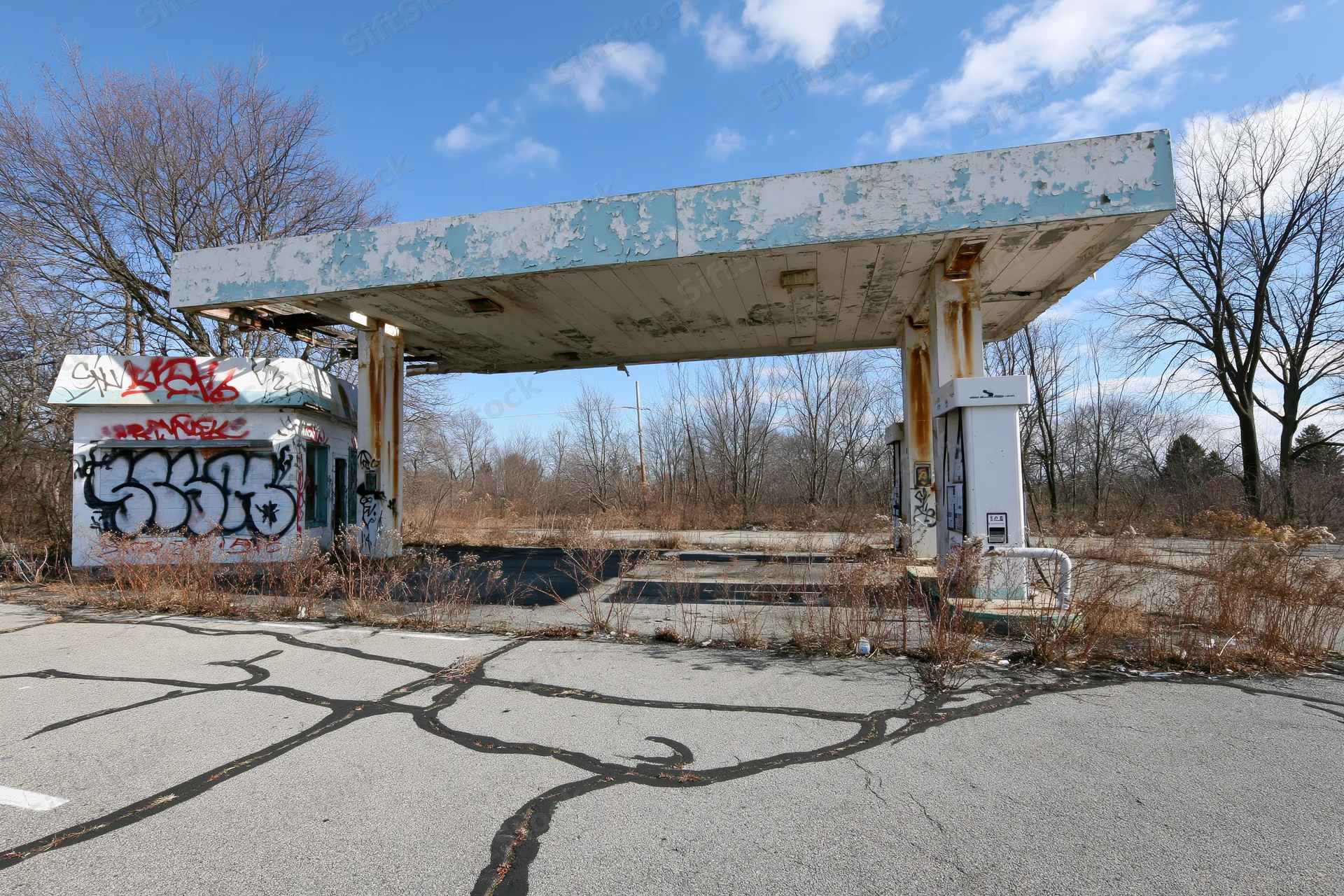Abandoned gas station with crumbling canopy and graffiti under a blue sky