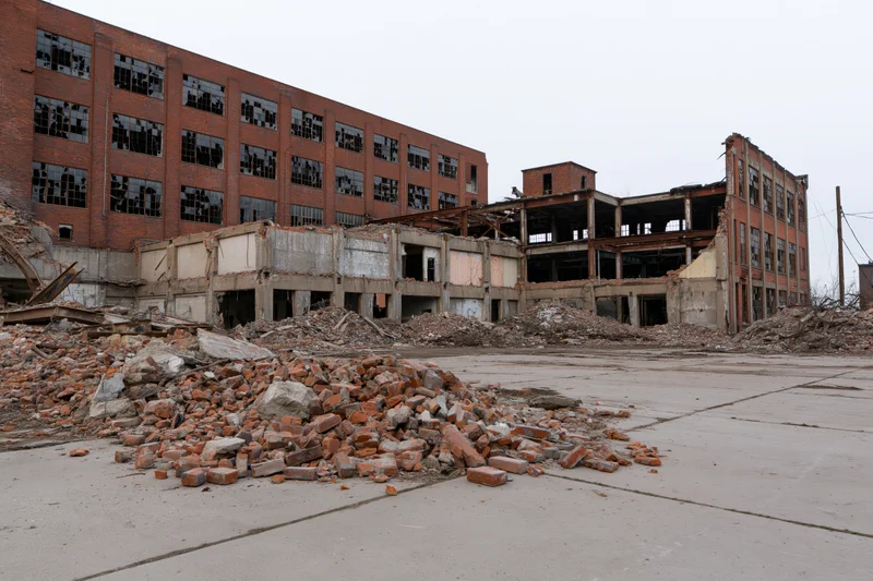 Abandoned industrial factory complex mid-demolition with piles of rubble and broken brick walls under overcast sky
