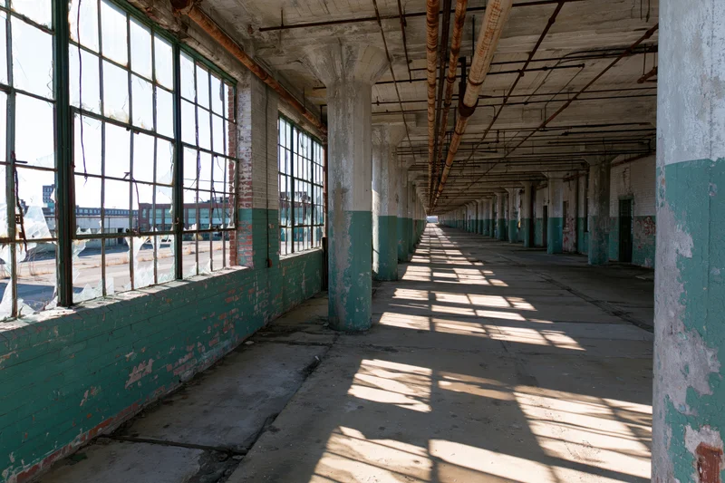 Long empty corridor in abandoned factory with sunlight streaming through broken windows