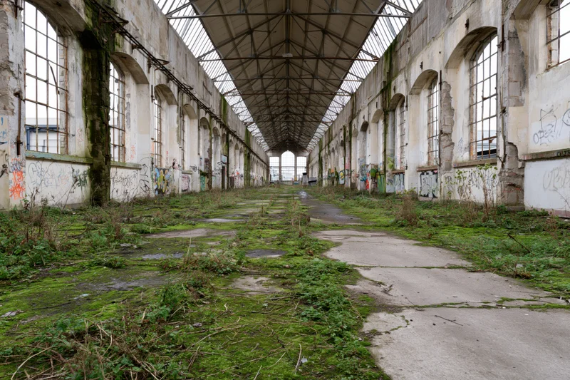 Long symmetrical interior of abandoned industrial factory hall with overgrown moss and graffiti on concrete walls and floor