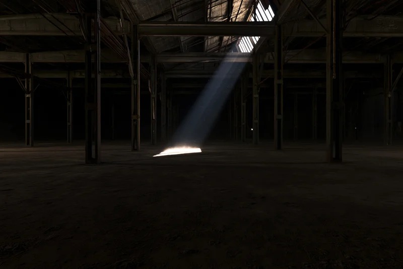 Abandoned industrial warehouse interior with sunlight streaming through skylight onto concrete floor