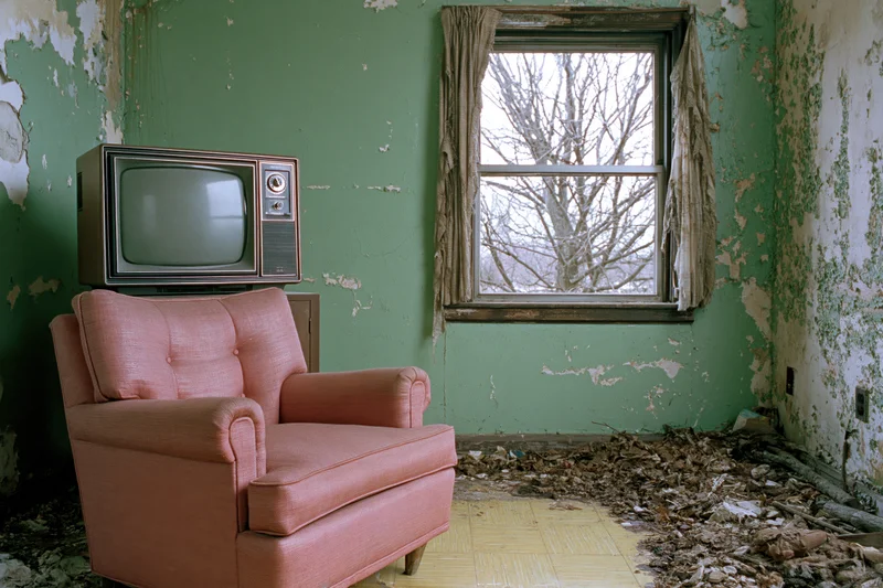 Vintage television on a pink armchair in an abandoned living room with peeling green walls and debris on the floor