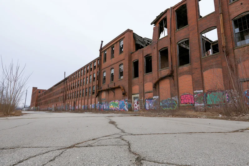 Long abandoned brick industrial factory complex with broken windows and graffiti on cracked pavement