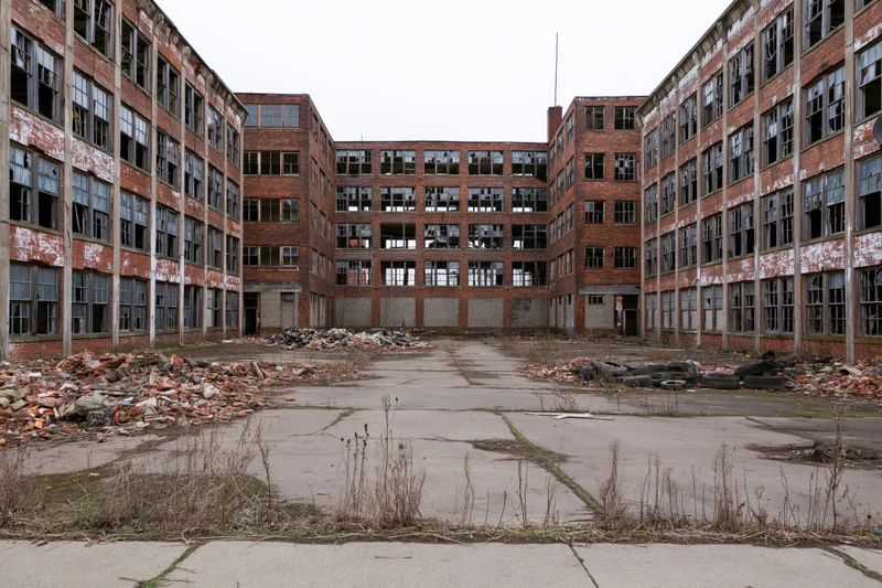 Abandoned industrial factory complex with crumbling brick buildings surrounding a debris-filled courtyard